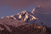 The rugged ridgeline leading up to the summit of Mt. Stroller White shines in the late afternoon winter light, with the peak's summit in the upper right hand corner just barely obscured by a colorful band of clouds.  Notice how the glow of the clouds lends its' colors to the tree covered mountainside below the peak.